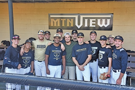 John Paul Kakos (center in green) stands on set flanked by fellow Mountain View teammates and cast members as they prepare to shoot a scene in the Bears’ dugout.