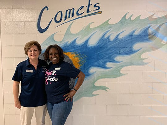 Principal Melissa Madsen and Gayle Middlebrook, a former student and current employee at Britt Elementary, show their Comet pride in the school's hallway.