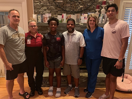 John Newsome stands in his living room with family, friends and neighbors who helped save his life. L-R: David Kittner (next-door neighbor); Maureen “Moe” Kittner, Flight Nurse with Critical Care Certification working for Angel MedFlight; Giovanni Newsome, Freshman football player at Athens Academy; John Newsome; Tracy Salas, Respiratory Therapist at Piedmont Atlanta Hospital, and Jesse Salas, a Senior at Brookwood High School. As a neighborhood lifeguard, Jesse helped perform CPR on John.