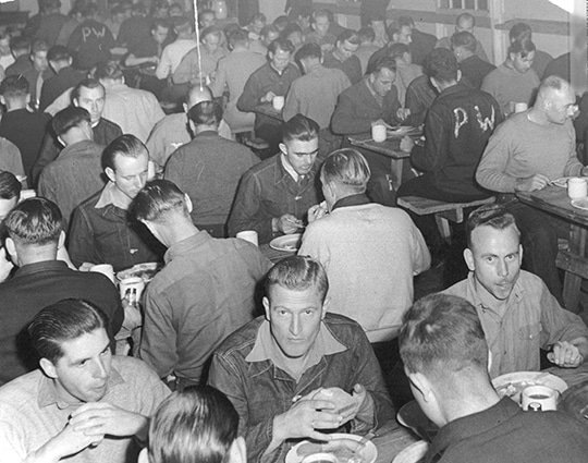 Prisoners of War eating in dining hall at a camp.