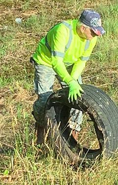 Dennis Swessel, co-founder, along with his wife, Donna, of the Blight Busters of Gwinnett, works hard to get rid of a dumped tire on the roadside.
